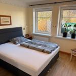 Schlafzimmer mit Bett, Fenstern und Pflanzen.