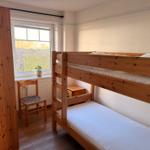 Zimmer mit Doppelstockbett, Holzstuhl und Fenster mit Blick auf Garten.