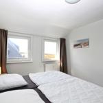 Schlafzimmer mit Doppelbett, zwei Fenstern und Kleiderschrank.