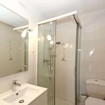 Badezimmer mit Dusche, Waschbecken und Toilette. Weiße Fliesen und Spiegel.