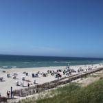Strand mit weißen Sand, bunten Strandkörben und Menschen unter blauem Himmel.