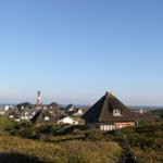 Dorf mit strohgedeckten Häusern und Leuchtturm am Horizont