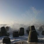 Wellen brechen an Betonblöcken am Strand.