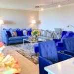 Wohnzimmer mit blauen Sesseln, Sofa und Glas-Tisch. Dekoration mit Blumen und Lampen.