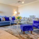 Wohnzimmer mit blauem Sofa, violettem Sessel und Glas-Tisch.