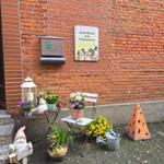 Willkommensschild an Backsteinwand mit Blumen, Stuhl und Gartendekoration.