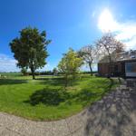 Hinterhof mit Grünfläche, Bäumen und Gartenmöbeln. Im Hintergrund sind Felder und Schafe sichtbar.