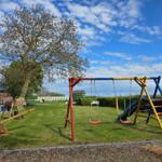 Kinderspielplatz mit Schaukel, Rutsche und Klettergerüst auf grünem Rasen.