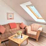 Wohnzimmer mit Sofa, Sessel und Tisch unter Dachschrägen mit Dachfenster.