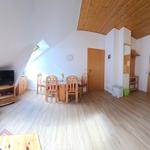 Wohn- und Essbereich mit Holzboden, Dachschrägen und TV. Essgruppe mit Tisch und Stühlen.
