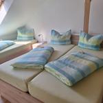Zwei Einzelbetten mit blau-gelben Decken und Kissen in einem Dachzimmer mit Holzrahmen.