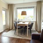 Esszimmer mit Tisch, Stühlen und Fenster. Vorhang, Pflanze und Schrank sichtbar.