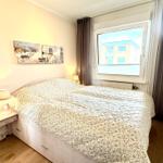 Schlafzimmer mit Doppelbett, Nachttisch und Fensterblick auf Gebäude.