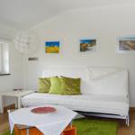 Ein Wohnzimmer mit weißem Sofa, grünen Kissen und Holzboden. An der Wand hängen drei Bilder.