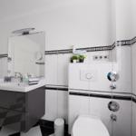 Badezimmer mit Waschbecken, Spiegel, Toilette und Dusche. Weiße Fliesen mit schwarzen Akzenten.