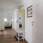 Flur mit Holzboden, Spiegel, Garderobe und Blick in Schlafzimmer und Wohnbereich.