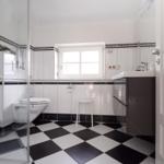 Badezimmer mit Dusche, Toilette und Waschbecken. Schwarze und weiße Fliesen.