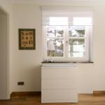 Ein Raum mit weißem Schrank, Fenster und Bild an der Wand.