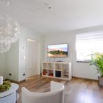 Wohnzimmer mit TV, Sofa, Stuhl und Pflanze. Holzboden und weißer Schrank.