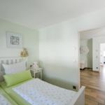 Schlafzimmer mit Doppelbett, grünen Kissen und Bildern an der Wand. Durchgang zu Wohn- und Küchenbereich.