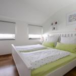 Ein Schlafzimmer mit Doppelbett, zwei Fenstern und einer TV-Wand