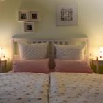 Schlafzimmer mit Doppelbett, zwei Nachttischen und Lampen. Wandbilder über dem Bett.
