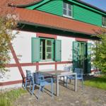 Haus mit grünen Fenstern und Terrasse mit Tisch und Stühlen.
