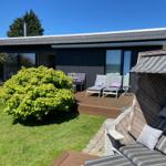 Terrasse mit Liegestühlen und Sonnenschutz, Grünfläche und modernes Haus im Hintergrund.