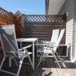 Terrasse mit Tisch und Stühlen, umgeben von Holzgeländern und Backsteinwand.