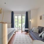 Ein Raum mit Sofa, Bett und Terrassentür. Wandbilder und Stehlampe sind sichtbar.