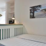 Schlafzimmer mit Bett, Wandbild und Lampe. Hintergrund zeigt Badezimmer.