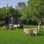 Garten mit Spielplatz, Trampolin und Holzmöbel unter Bäumen.