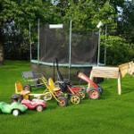 Garten mit Trampolin und bunten Kinderfahrzeugen.