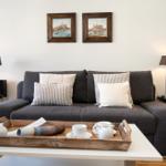 Ein Wohnzimmer mit grauem Sofa, zwei Bildern an der Wand und einem weißen Tisch.