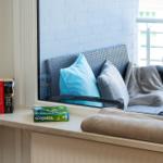 Blick auf eine Sitzecke mit Kissen und Decke. Auf der Fensterbank liegen Bücher und ein Scrabble-Spiel.