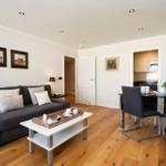 Wohnzimmer mit Sofa, Esstisch und Küchenbereich. Holzboden und Wandbilder.