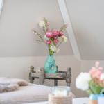 Schlafzimmer mit Blumenarrangement und Holztisch unter schrägen Deckenbalken.