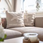 Ein Sofa mit Kissen, die Sterne und Text zeigen, vor einem Fenster mit Seepferdchen-Dekoration.