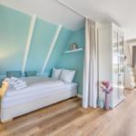 Schlafzimmer mit Bett, Schrank und Fenster. Wandfarbe mint. Holzfußboden.