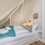 Schlafzimmer mit Dachschrägen, Bett mit Kissen und Decke, Wanddekoration und Nachttisch.