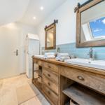 Badezimmer mit Holzwaschtisch, zwei Spiegeln und Dusche unter Dachschrägen.