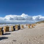 Strand mit Strandkörben und Wellen unter blauem Himmel mit Wolken.