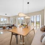 Dining area with wooden table and bench. Living area with sofa and windows.