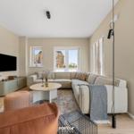 Living room with corner sofa, round table, and TV. Windows with view to outside area.