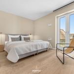 Bedroom with bed, nightstand, and chair. Window with view of rooftops.