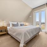 Bedroom with bed, nightstand, and window. Wooden floor and beige walls.