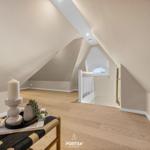 Attic with wooden floor, white walls, and a window. A small table with a candle and plant.