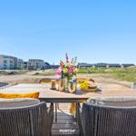 Terrace with table and chairs, view of modern buildings and dunes.