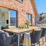 Terrace with dining table and chairs in front of brick house with thatched roof.