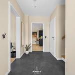Hallway with dark floor, plant, and view into kitchen.